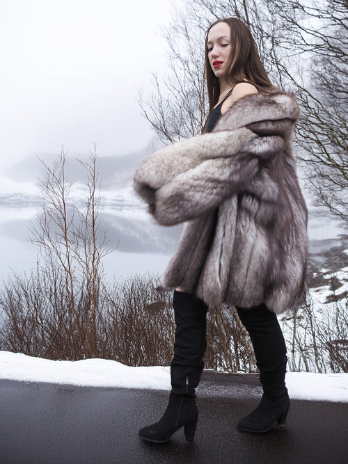 Real fur blue fox coat with natural silver tones, modeled on a snowy road. Plush and warm outerwear for luxury winter fashion.