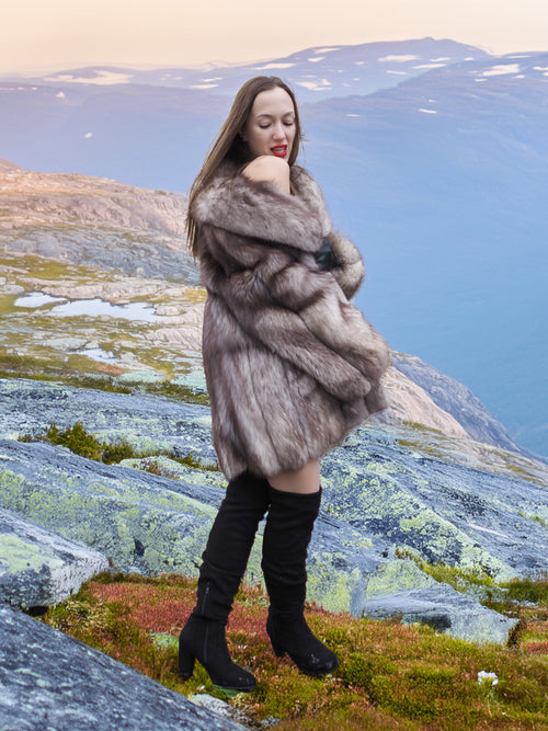Silver-blue fox fur coat with thick texture and elegant drape, worn in a rocky mountain landscape. High-end fur fashion for winter.