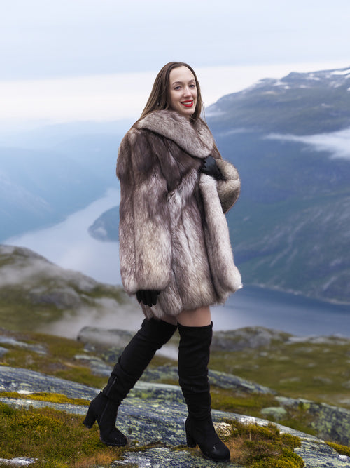 Luxury blue fox coat with plush fur and wide collar, modeled on a scenic cliff. Real fur outerwear for upscale winter style.