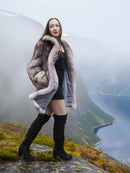 Plush soft blue fox coat with satin lining and wide collar, modeled on a misty cliffside. Real fur outerwear for luxury winter fashion.