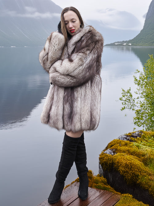 Brand new silver-blue fox fur coat with elegant drape and cozy fit, worn near a mossy lakeside. Real fur fashion outerwear in medium/large size.