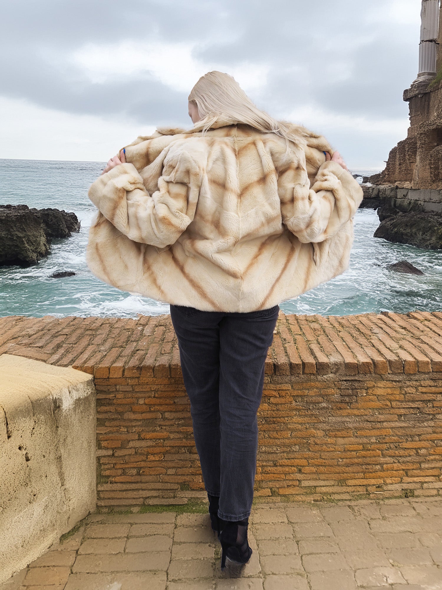 Back view of Reversible Versatile Sheared Mink Fur Jacket Coat S showing wide fur pattern, styled near rocky coastline.