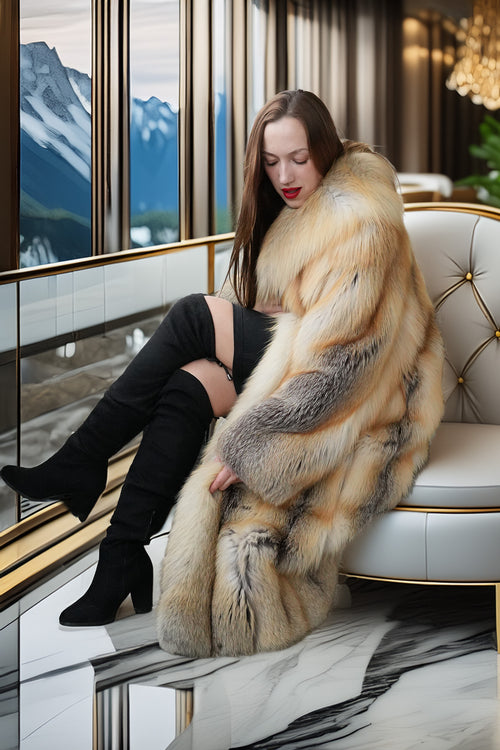 Woman in a fur coat sitting on a chair with a scenic view outside the window.