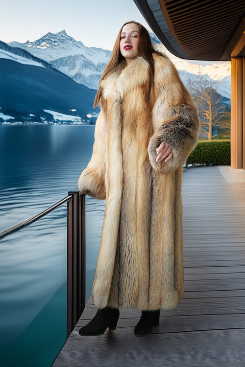 Woman in a fur coat standing on a deck with a scenic mountain and lake view.