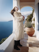 Woman in a fur coat standing on a balcony with a scenic ocean view