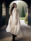 Woman wearing a long white fur coat standing in a garden.