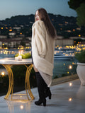 Woman in a fur coat standing on a rooftop with a cityscape at night.