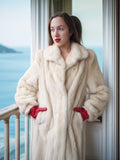 Woman wearing a white fur coat and red gloves standing on a balcony with a scenic view.