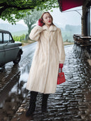 Woman in a fur coat and red gloves standing on a rainy street with a vintage car and cafe in the background.