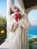 Woman in a fur coat and red gloves standing by a scenic coastal area.