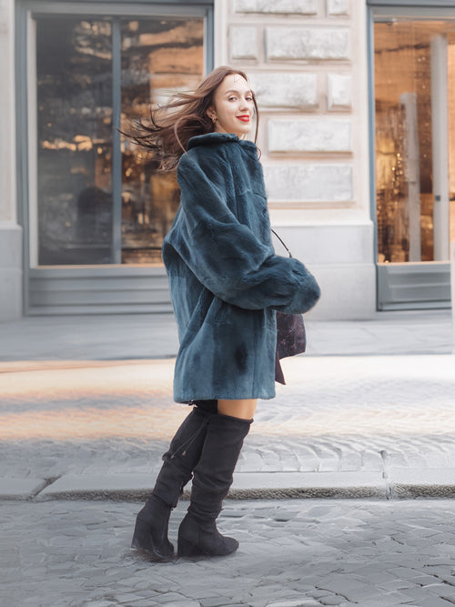 The Still Hour fur coat in deep teal sways as the model walks, highlighting its plush texture and stylish winter-ready design.