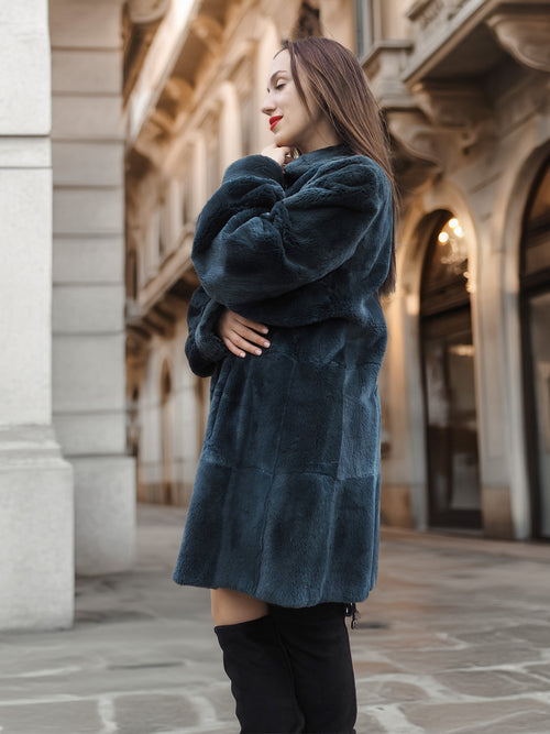 Side profile of The Still Hour sheared muskrat fur coat in deep teal, styled with black boots for a refined cold-weather look.