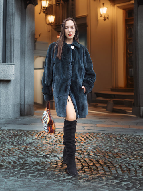 The Still Hour sheared muskrat fur coat in deep teal styled with a colorful handbag and black boots, ideal for upscale winter wear.