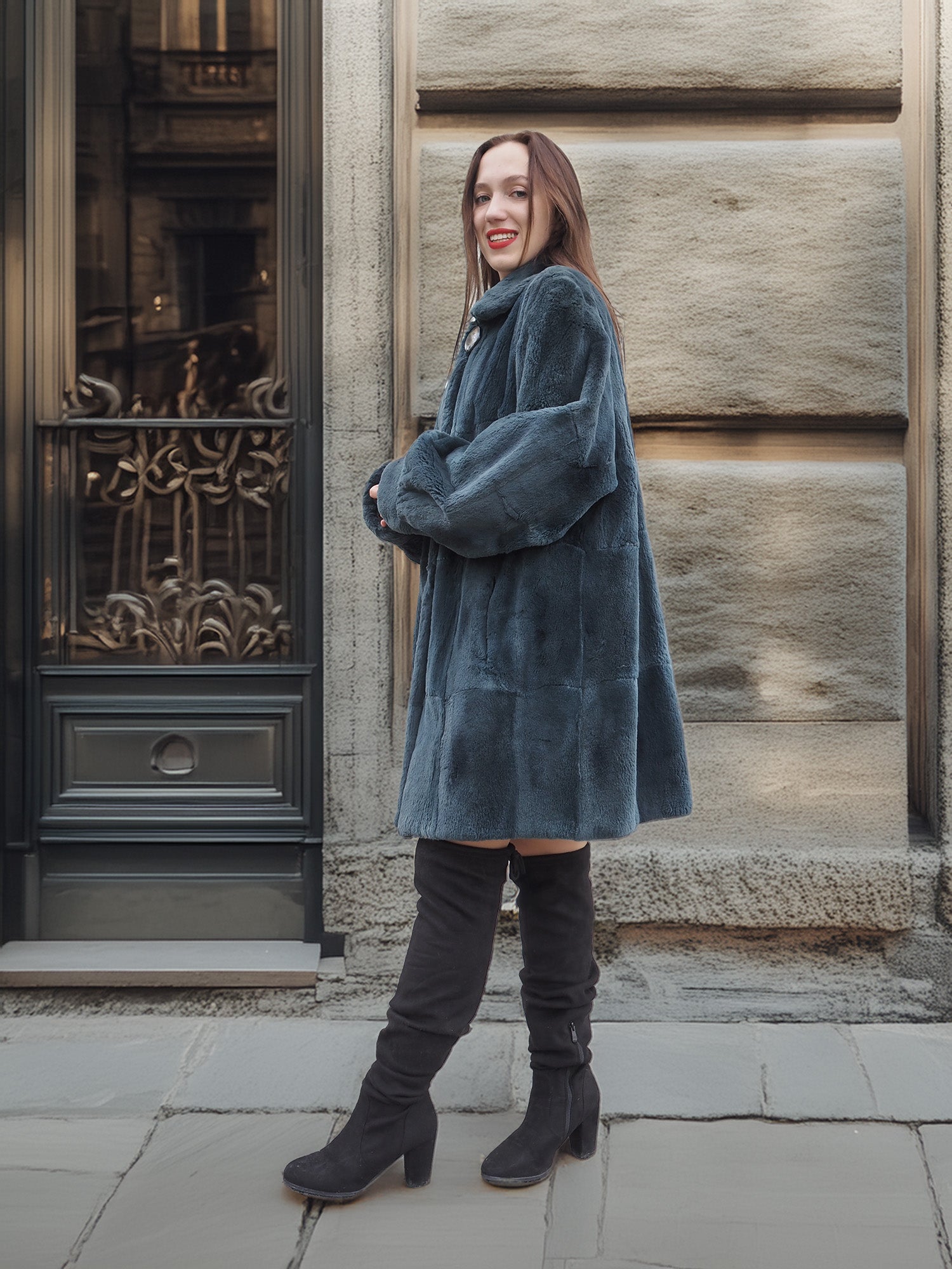 Model leans against stone wall in The Still Hour sheared muskrat fur coat in deep teal, styled for elegant winter outerwear fashion.