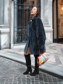 The Still Hour sheared muskrat fur coat in deep teal M/L styled with black thigh-high boots and a colorful handbag, perfect for luxury winter fashion.