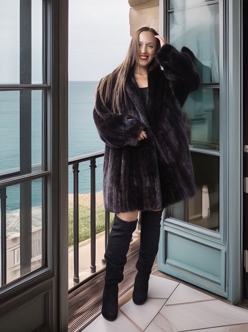 Woman in a black fur coat standing on a balcony with ocean view