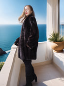 Woman in a dark fur coat standing on a balcony with a scenic ocean view.