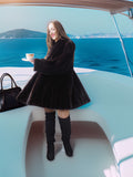 Woman in a black coat holding a cup on a boat with a scenic background