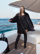 Woman in black coat and boots standing on a boat with ocean view