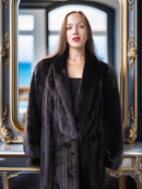 Woman wearing a dark fur coat in front of an ornate mirror with a blurred background
