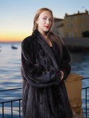 Woman in a fur coat standing by a waterfront at sunset