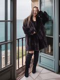 Woman in a black fur coat standing on a balcony with ocean view