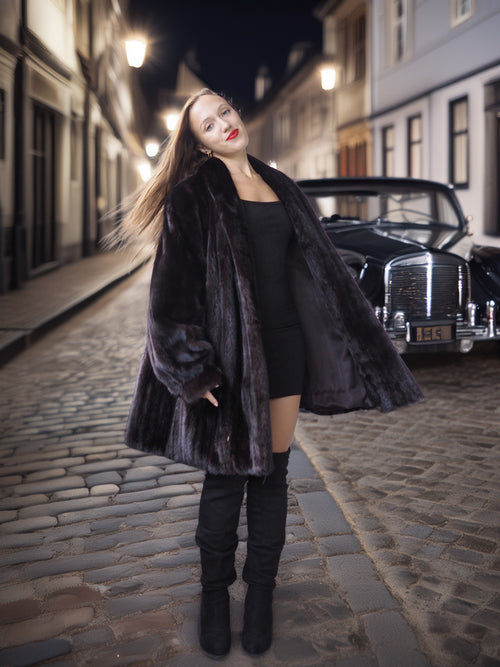 Woman in a fur coat standing on a cobbled street at night.
