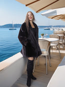 Woman in a black coat standing on a boat deck with water and boats in the background
