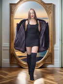 Woman in a black dress and knee-high boots standing in front of a large ornate mirror.
