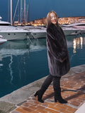 Woman in a fur coat standing by a marina at night