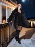 Woman in a black coat standing on a balcony at night with a moonlit view.
