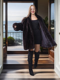 Woman in a dark fur coat standing on a wooden deck with ocean view