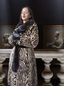 Woman wearing a leopard print coat in an artistic setting with classical sculptures.