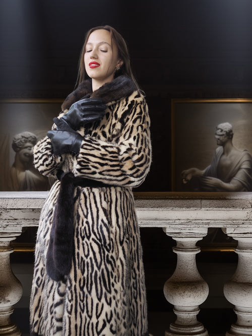 Woman wearing a leopard print coat in an artistic setting with classical sculptures.