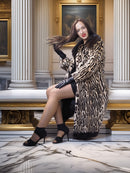 Woman in a leopard print coat sitting on a marble bench in an elegant interior setting.