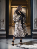 Woman in a leopard print coat standing in an elegant interior setting