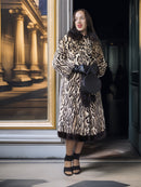 Woman in a leopard print coat standing in a doorway with a painting in the background