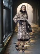Woman in a leopard print coat standing in a sunlit archway.
