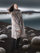 Person wearing a fur coat standing in a surreal landscape with mountains and water.