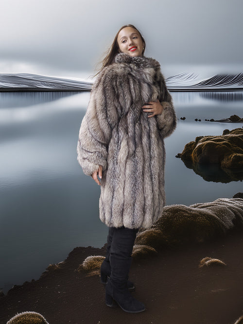Person wearing a fur coat standing by a reflective body of water.
