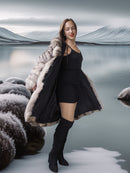 Woman in a black dress and fur-trimmed coat standing in a snowy landscape.