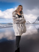 Woman in a fur coat standing on a beach with mountains in the background