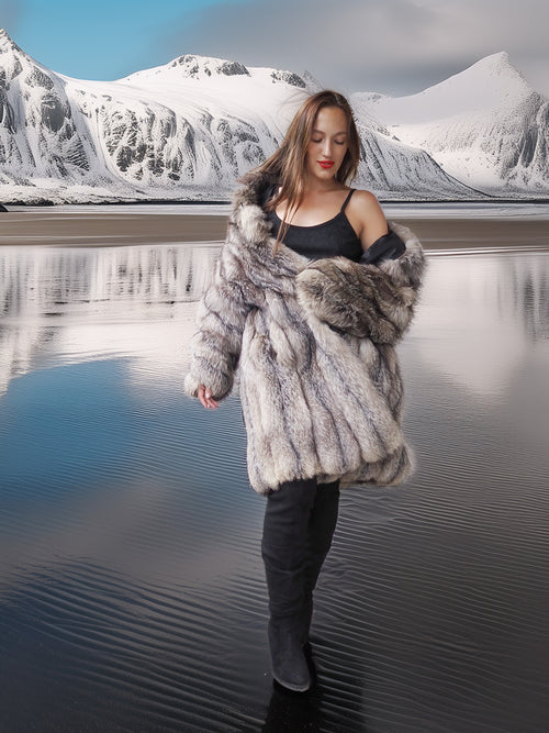 Woman in a fur coat standing in front of a snowy mountain landscape