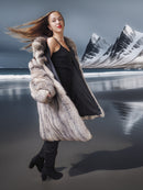 Woman in a fur coat and black dress standing in front of a mountainous landscape.
