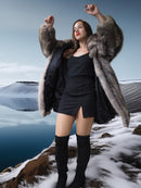 Woman in a fur coat and black outfit standing on a snowy landscape with a lake in the background