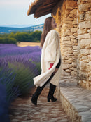 Woman in a white cardigan standing in front of a stone building with lavender fields in the background