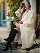 Woman in a fur coat sitting at an outdoor cafe table with a cup of coffee.