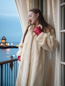 Woman in a fur coat and red gloves standing on a balcony with a scenic view of water and lights.