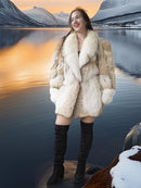 Woman in a fur coat standing by a lake with mountains in the background