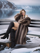 Woman in fur coat and knee-high boots sitting on a bench by a snowy landscape